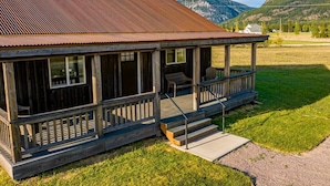 A rustic wooden cabin with a metal roof, a porch with steps, and a view of mountains in the background.