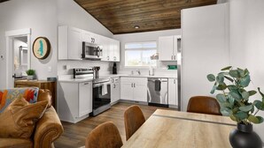 A modern kitchen with white cabinets, a microwave, and a dishwasher. There is a dining area with a wooden table and chairs.