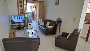 Un salon avec une table basse en verre, deux canapés en cuir, un téléviseur et un ventilateur.