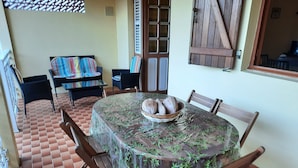 Une table de salle à manger ronde, recouverte d’une nappe transparente, est entourée de chaises en bois. Un panier de pain est posé sur la table.