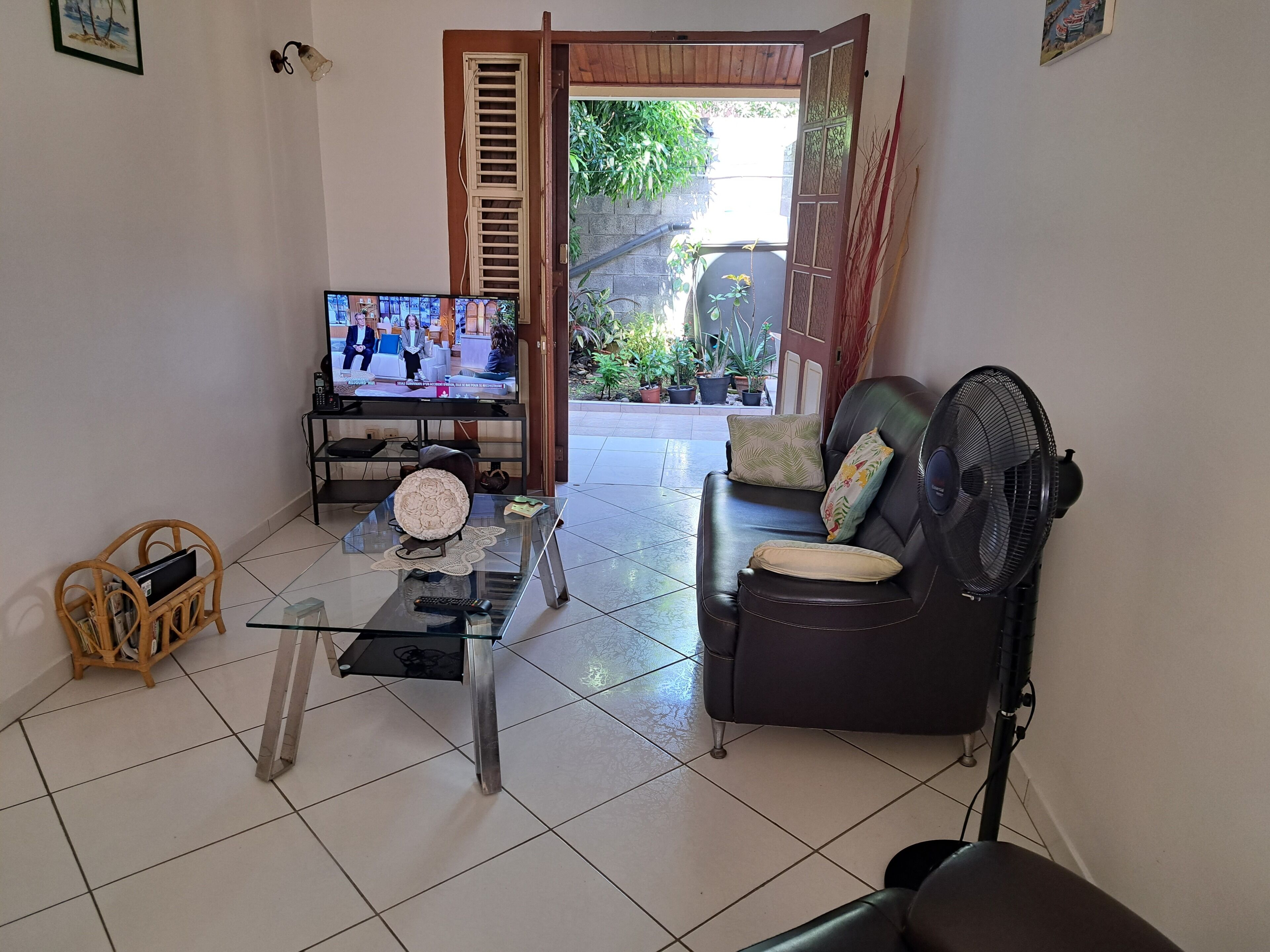 A living room with a glass coffee table, a leather sofa, a television, and a fan.
