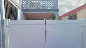 A white gate with a decorative lattice on top, leading to a building with a balcony. - Rustic Private Studio  (Toa Baja)