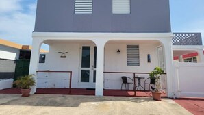 A two-story building with a flat roof, a covered patio area with outdoor seating, and a small entrance with a glass door. - Rustic Private Studio  (Toa Baja)
