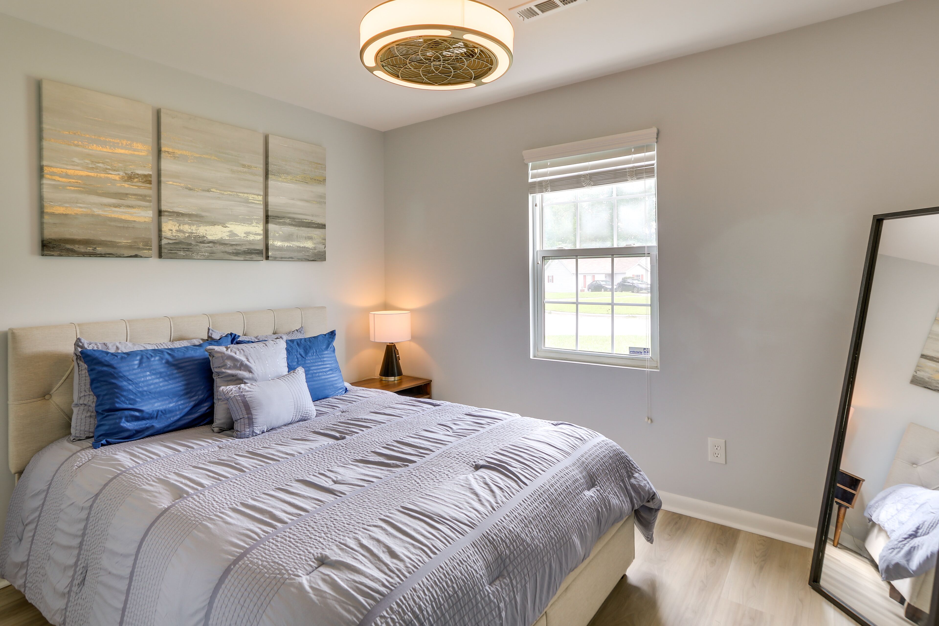 A bedroom with a large bed, a nightstand, a lamp, a window, and a mirror.