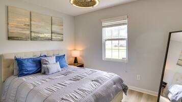 A bedroom with a large bed, a nightstand, a lamp, a window, and a mirror.