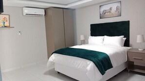 Habitación de hotel ordenada con cama, mesitas de noche, aire acondicionado instalado en la pared y un cuadro enmarcado.