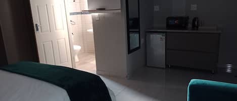 A hotel room with a bed, a desk, a television, and a small kitchenette.