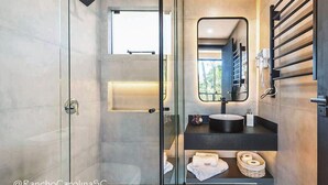 A modern bathroom with a glass shower enclosure, a built-in sink with a black countertop, and a mirror above the sink. - Rancho Carolina (Rancho Queimado)