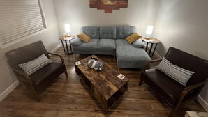 Een woonkamer met een hoekbank, twee fauteuils, een salontafel en twee bijzettafels met lampen.