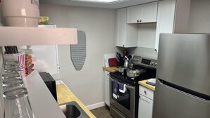 Een compacte keuken met witte kastjes, een roestvrijstalen koelkast, een fornuis en een magnetron. Er is een houten aanrechtblad en een spoelbak met een metalen rek.