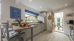 A modern kitchen with white cabinets, a wooden countertop, and a window with blue blinds. - Miramare Cottage,  Holme-next-the-Sea, Norfolk (Holme-next-the-Sea)