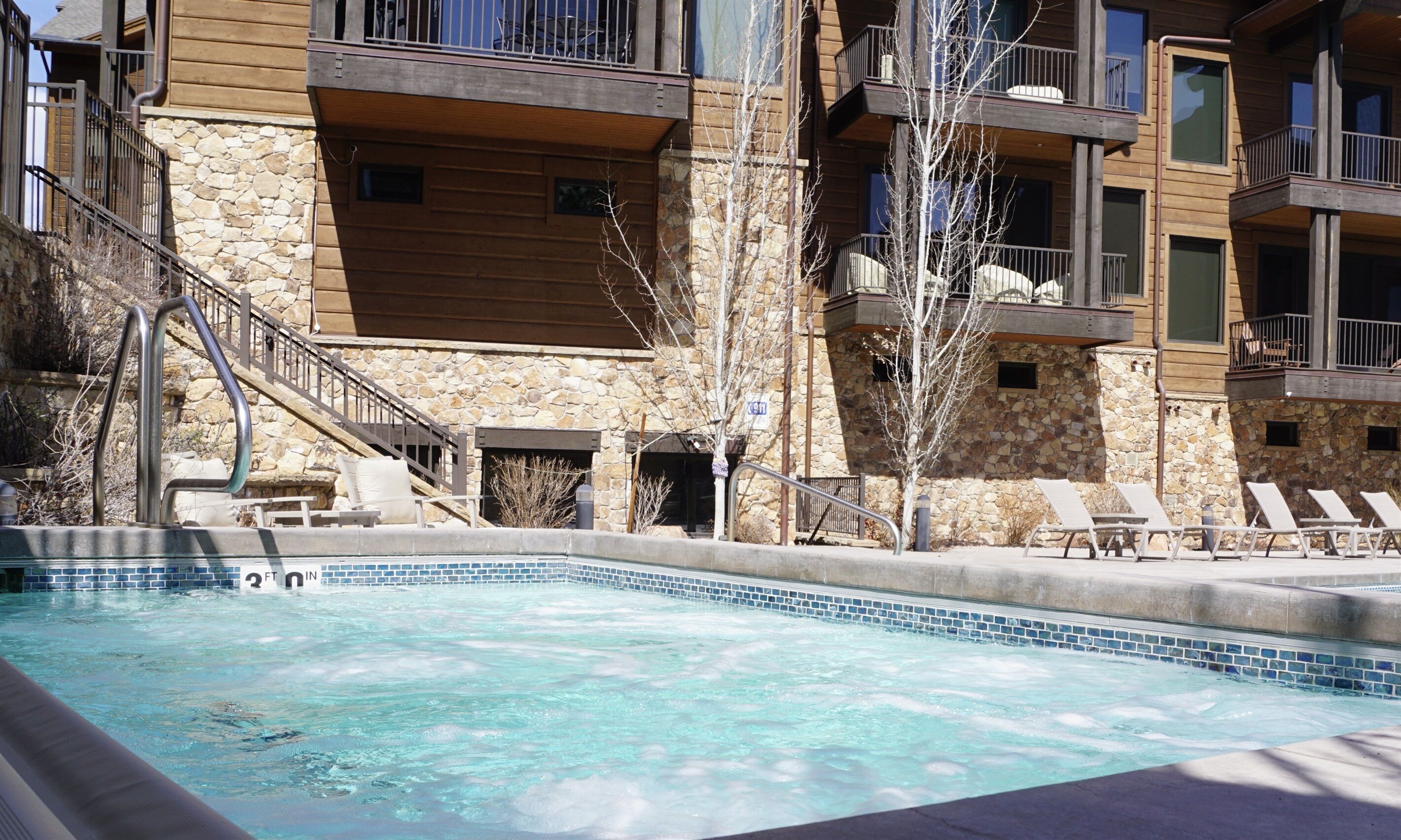 A hotel with a stone facade, a swimming pool, and outdoor seating.