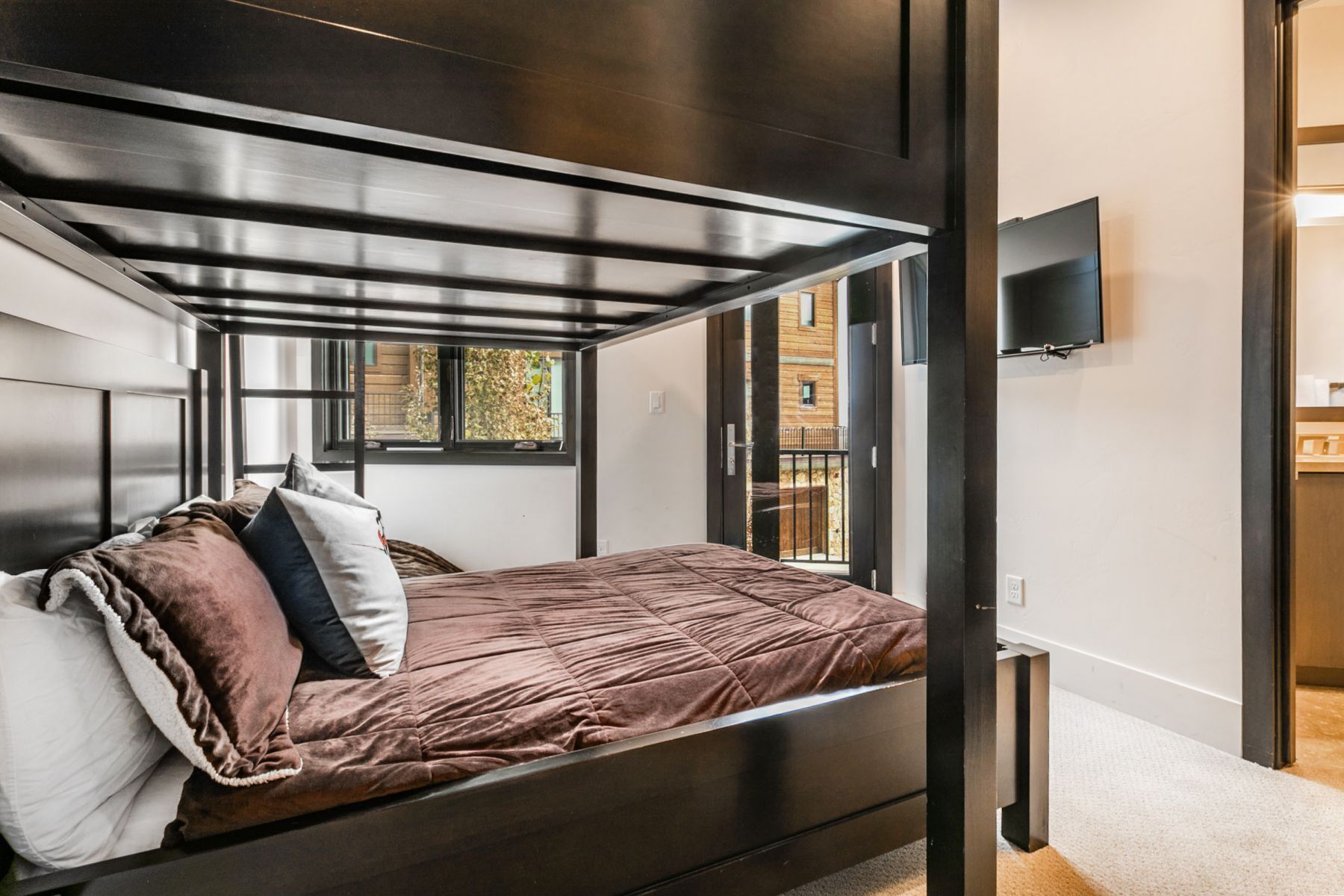 A modern bedroom with a bunk bed, a window with a view of a building, and a flat-screen TV mounted on the wall.