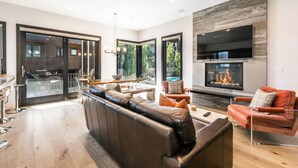 Una sala de estar moderna con chimenea, sofá de cuero y comedor con ventanas amplias.