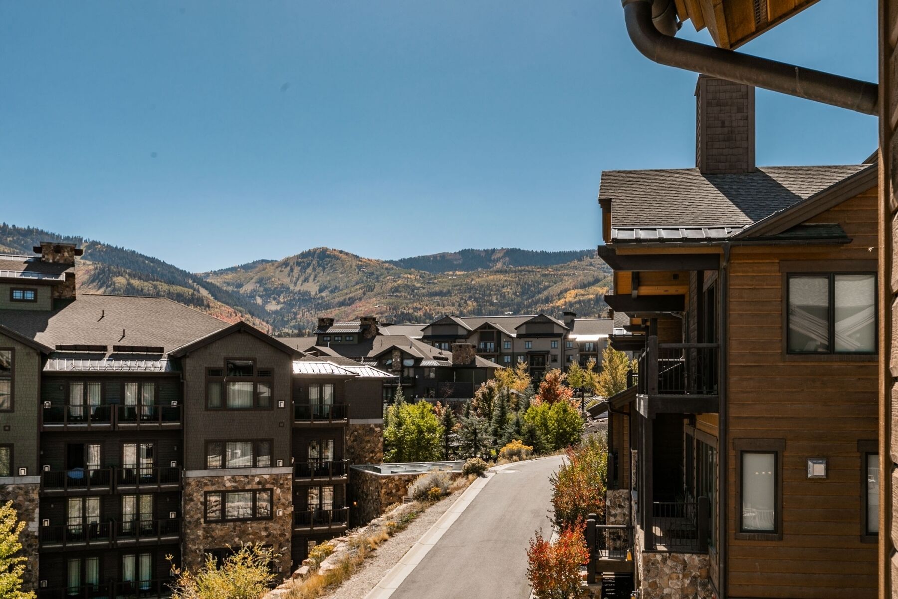 A row of modern multi-story buildings with stone facades, a central road, and a mountainous backdrop.