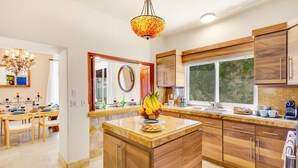 A modern kitchen with wooden cabinets, a central island with fruit, and a large window. - Villa Cola de Ballena Luxury Villa with ARCADE Room, El Pedregal. Security 24/7 (Cabo San Lucas)