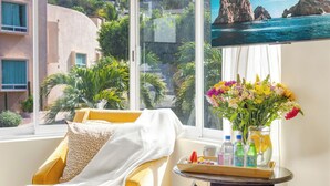 A room with a yellow armchair, a small table with a tray of drinks and a vase of flowers, and a window with a view of a rocky coastline. - Villa Cola de Ballena Luxury Villa with ARCADE Room, El Pedregal. Security 24/7 (Cabo San Lucas)