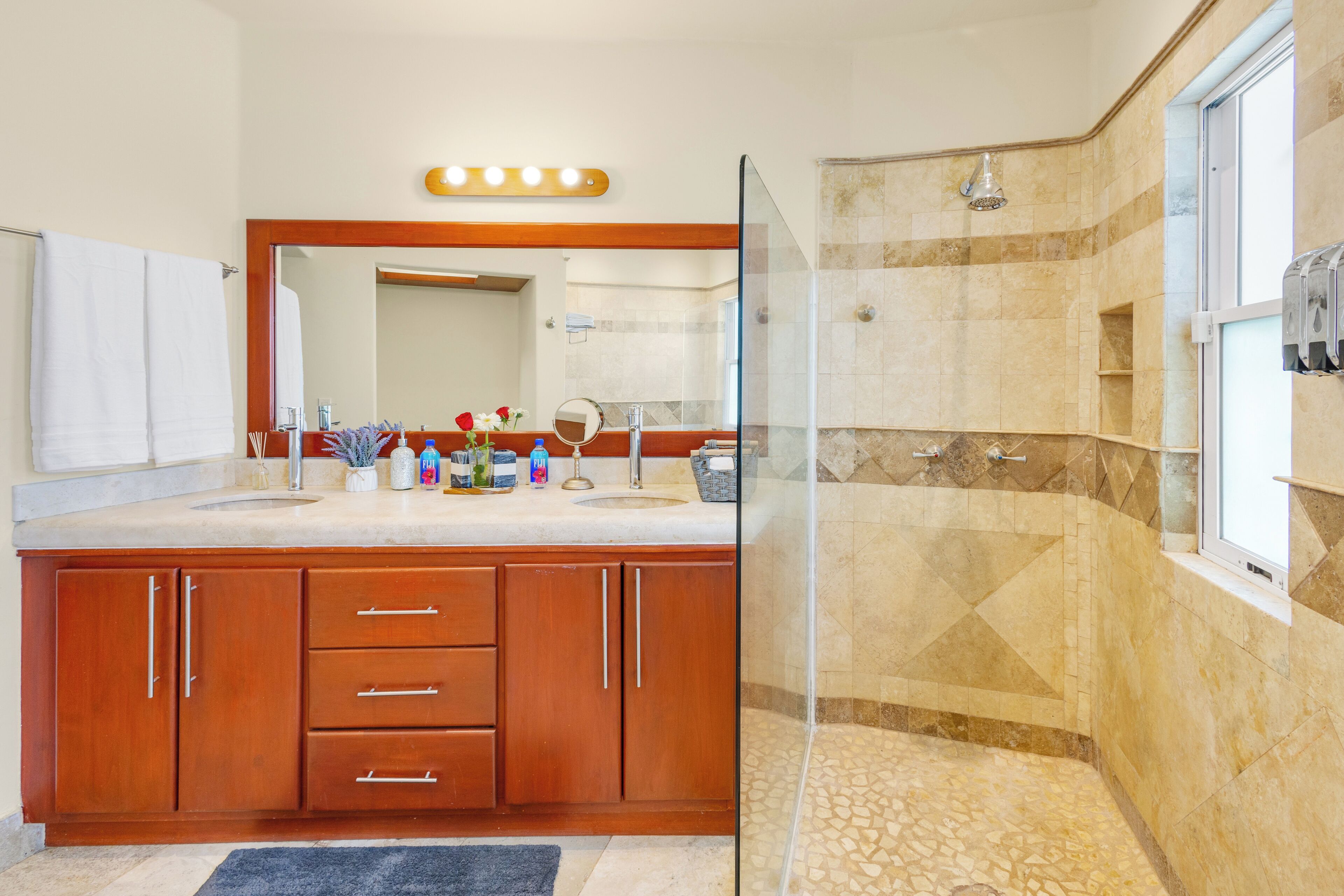A modern bathroom with a glass-enclosed shower, wooden cabinetry, and a vanity with a mirror and toiletries.