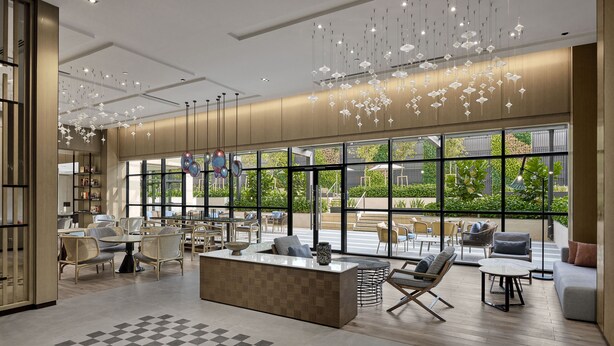A modern interior with a central reception desk, seating areas, and large windows offering views of greenery.