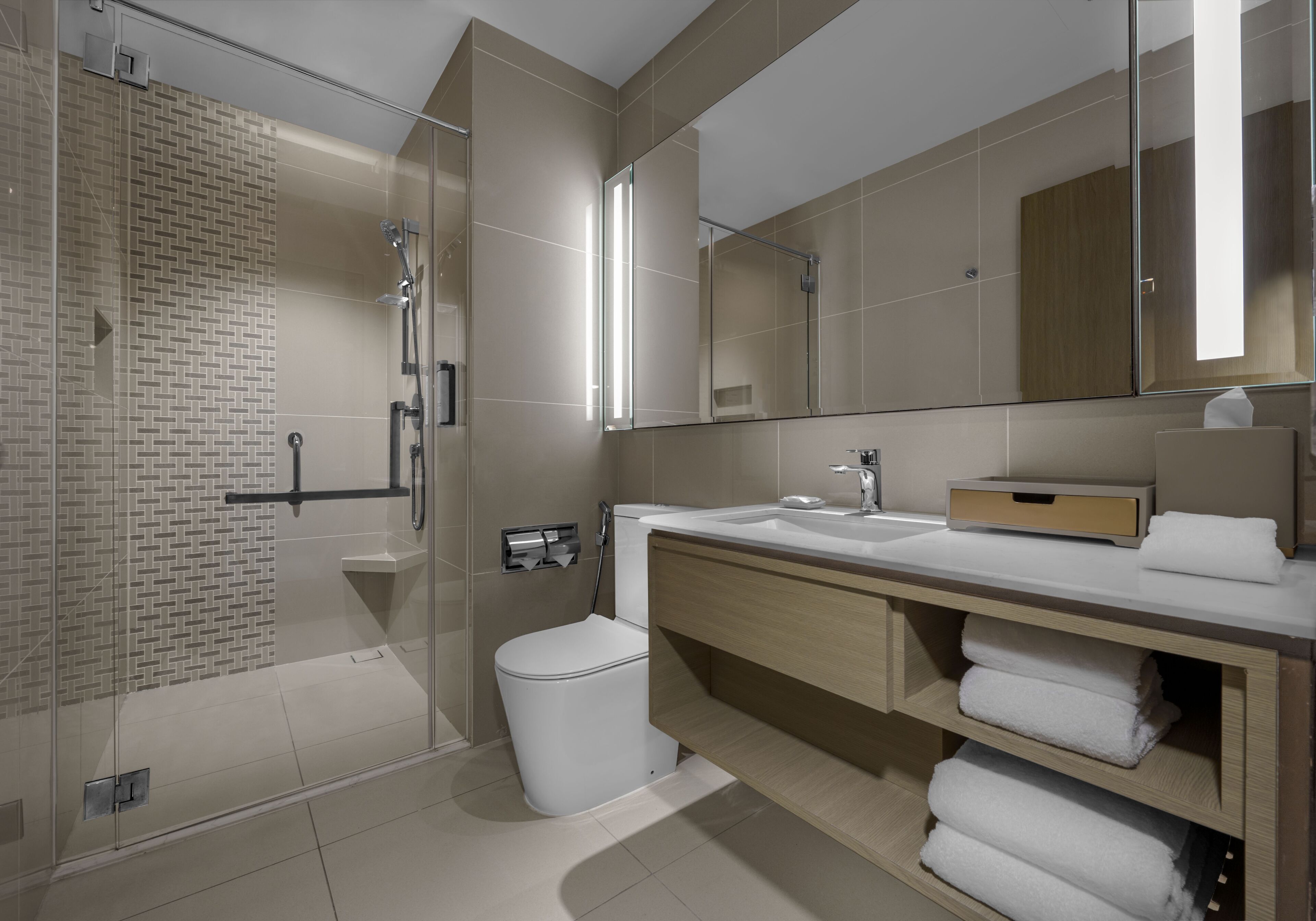 Un baño moderno con cabina de ducha de vidrio, inodoro y tocador con espejo y perchero.