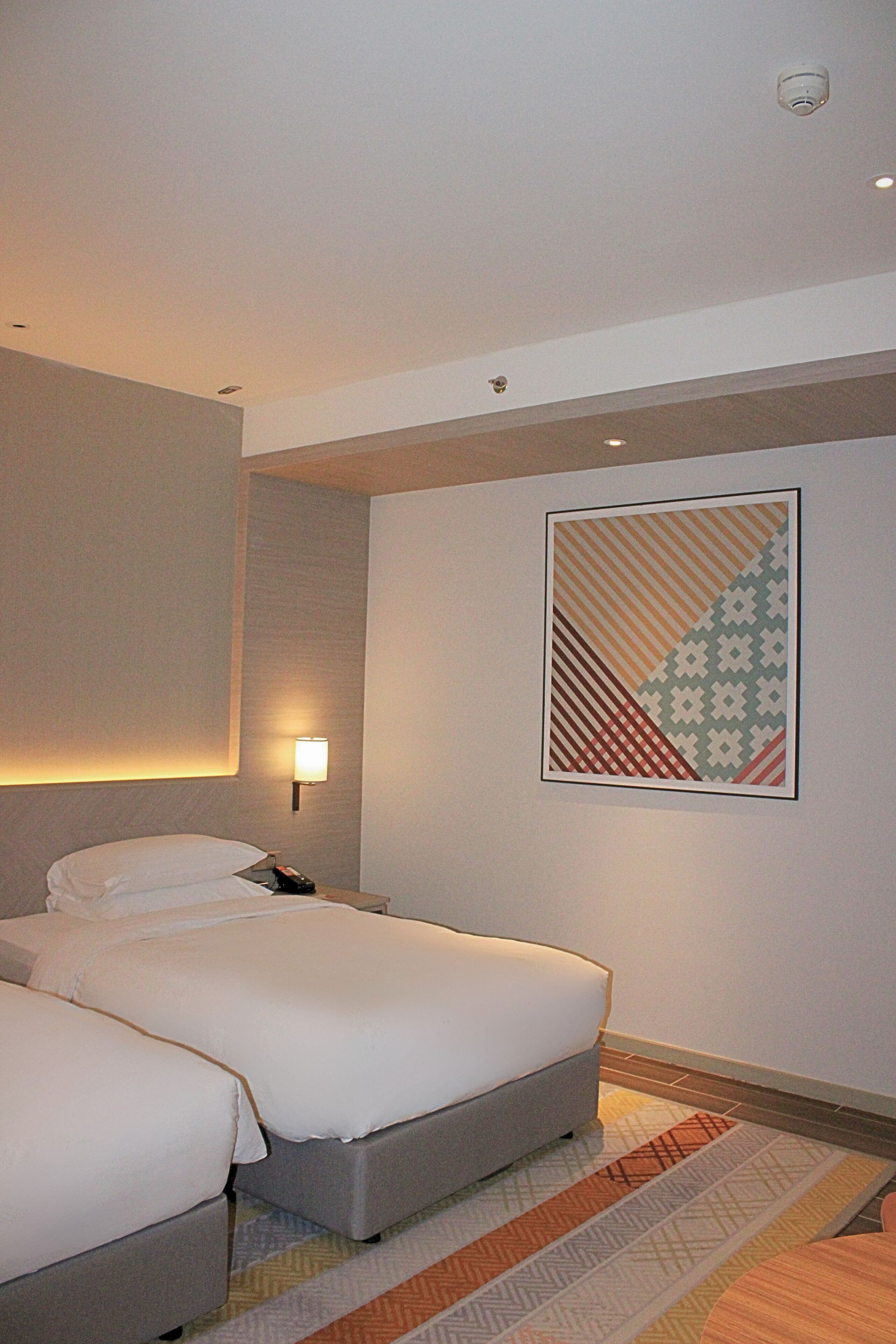 A hotel room with two beds, a wall-mounted lamp, and a patterned artwork.