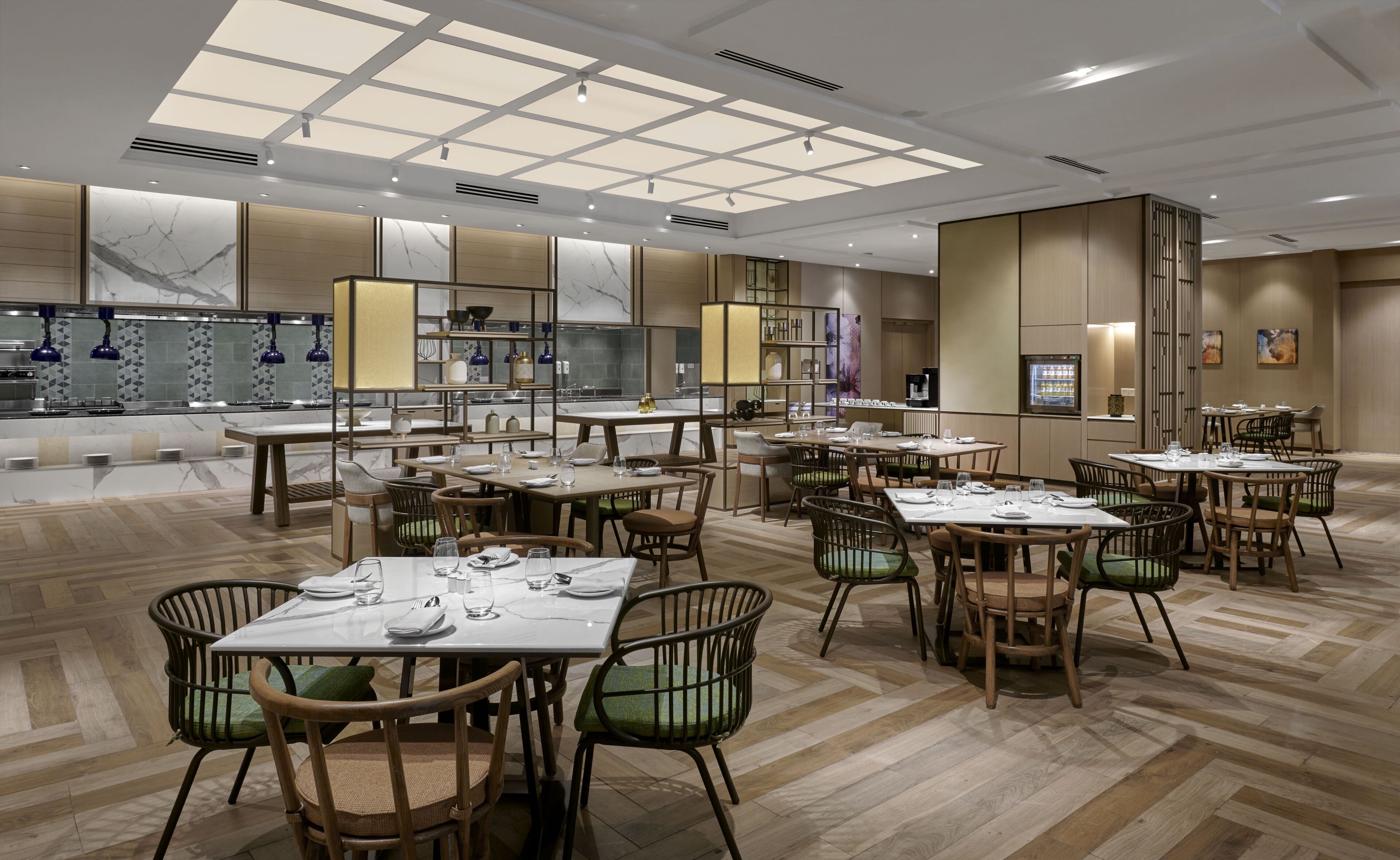 A modern restaurant with multiple dining tables and chairs, a kitchen area, and a ceiling with skylights.