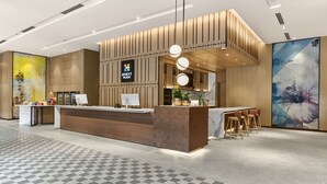 A modern hotel reception area with a wooden reception desk, a digital display, and a bar area with stools.