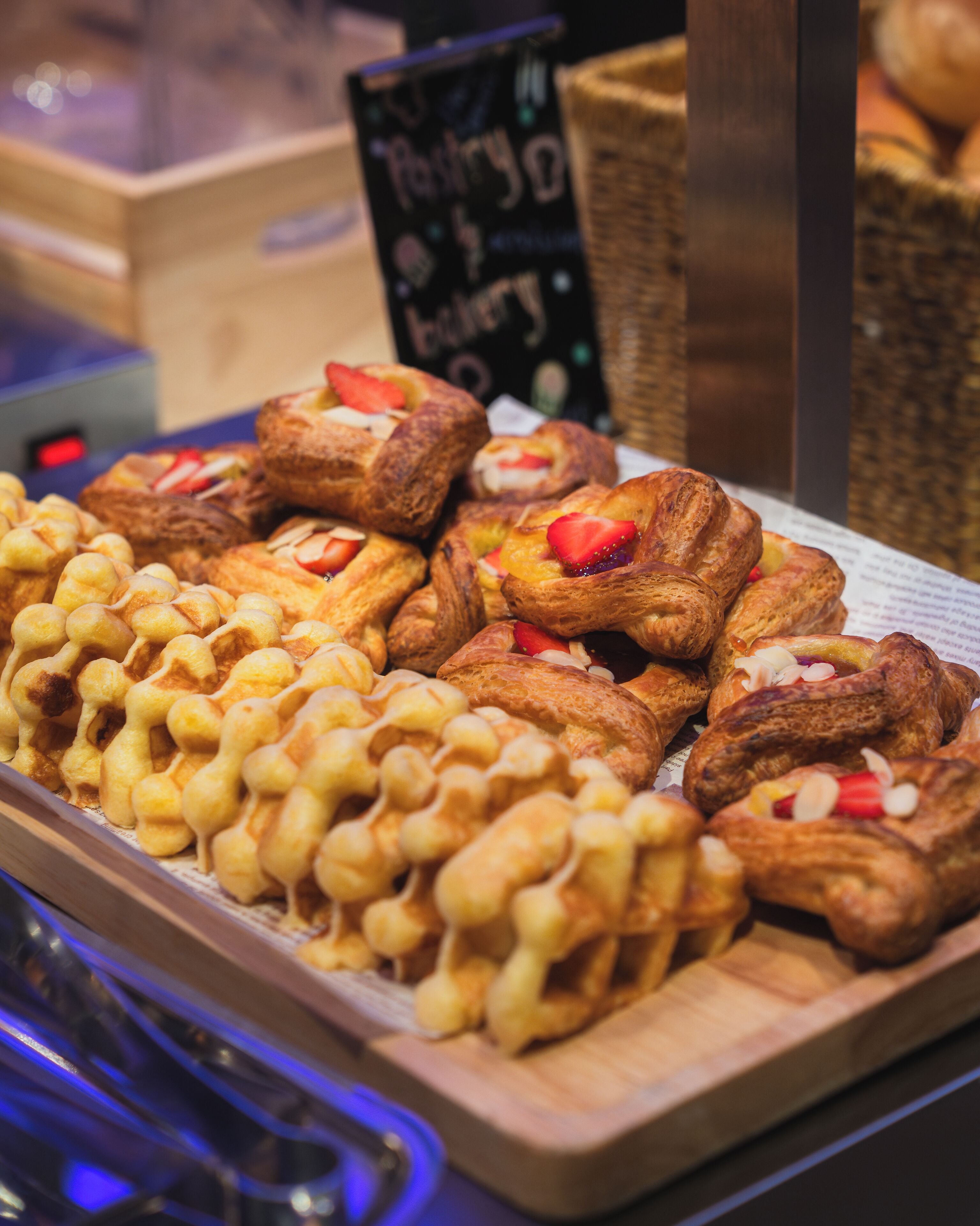 A display of assorted pastries, including waffles and pastries topped with fruits and nuts, arranged on a wooden board.