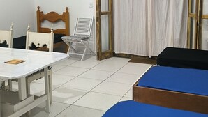 Une chambre avec deux lits, une table, une chaise, un ventilateur de plafond et une fenêtre avec des rideaux.