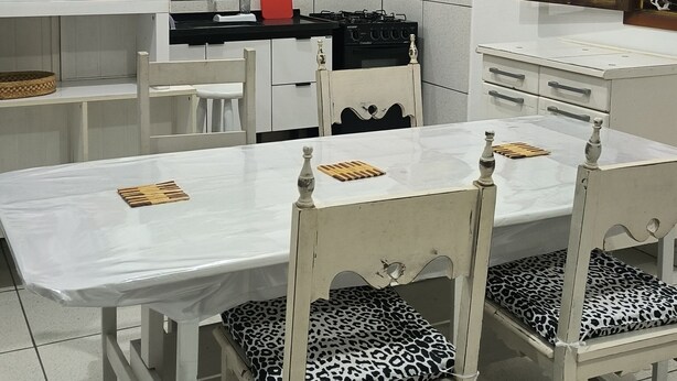 Un coin repas avec une table et des chaises blanches, une cuisine en arrière-plan et un tableau coloré accroché au mur.