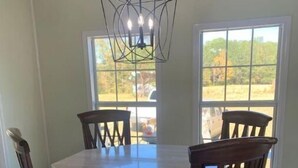 Un comedor con una mesa redonda, cuatro sillas de madera con asientos acolchados y una lámpara de techo geométrica.