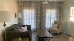Una sala de estar con sofá, sillón, mesa de centro y cortinas.