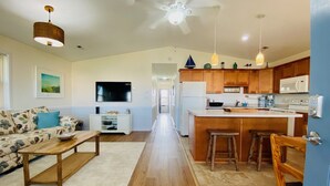 A modern kitchen with wooden cabinets, a central island, and a dining area with a sofa and coffee table. - "Claire Skies" 75 yards to Beach access! (Nags Head)