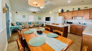 A spacious kitchen with wooden cabinets, a central island, and a dining area with a long wooden table and chairs. - "Claire Skies" 75 yards to Beach access! (Nags Head)