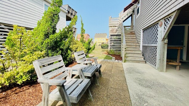 A pathway with wooden benches, surrounded by greenery and a building with a wooden deck. - "Claire Skies" 75 yards to Beach access! (Nags Head)