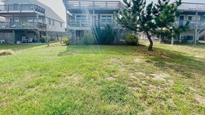 A residential area with a grassy yard, a wooden fence, and a multi-story building with balconies. - "Claire Skies" 75 yards to Beach access! (Nags Head)