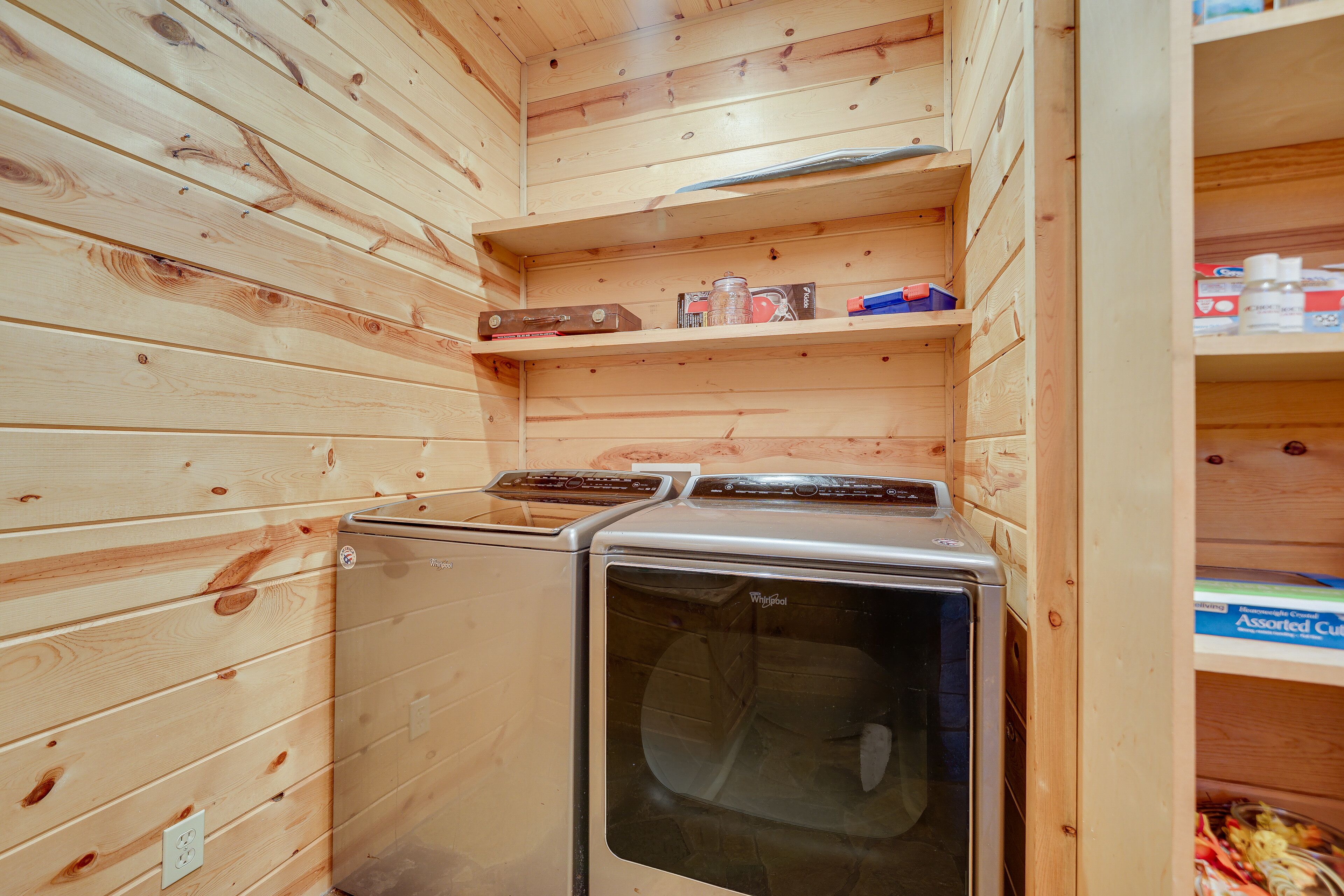 A compact laundry room with wooden walls and shelves containing cleaning supplies.