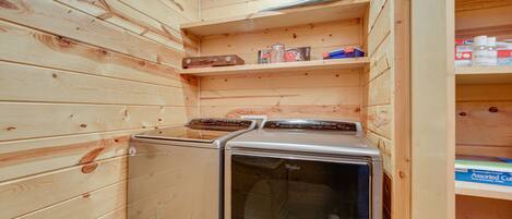 A compact laundry room with wooden walls and shelves containing cleaning supplies.