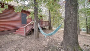Een rustieke houten hut met een terras en een hangmat tussen de bomen.