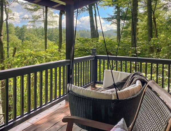 A covered outdoor deck with wicker furniture and a view of a forested landscape. - Leaf & Log Serene Cabin w/ Lounge Deck & Firepit (Cherry Log)