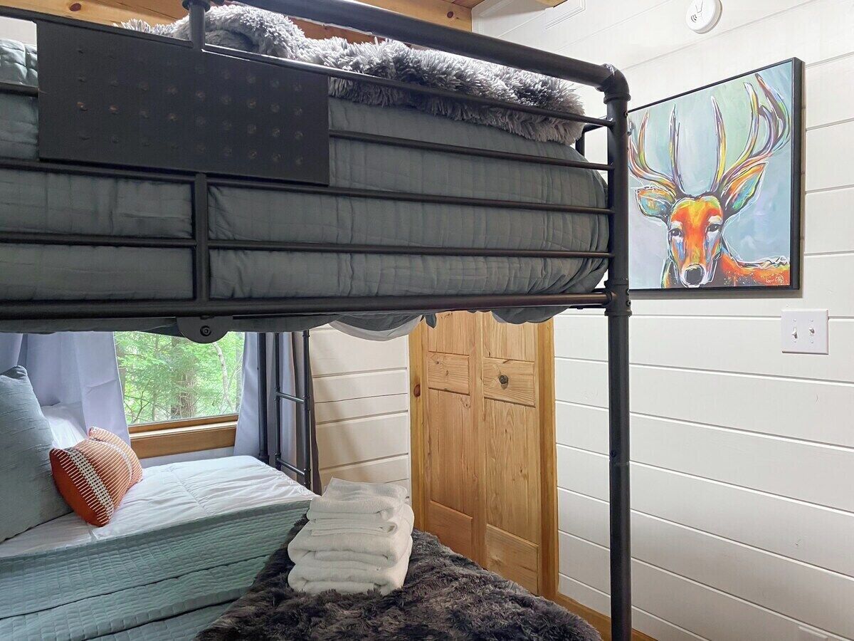 A bunk bed with a window, a wooden door, and a painting of a deer on the wall.