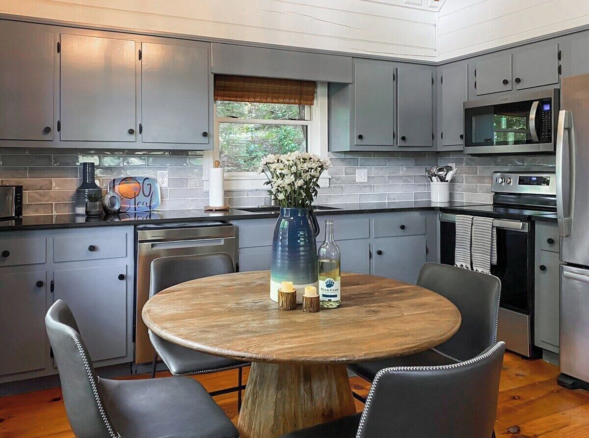 A modern kitchen with grey cabinets, a wooden dining table, and a vase with flowers.