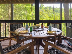 A wooden deck with a round table and chairs, surrounded by a railing, overlooking a forested area. - Leaf & Log Serene Cabin w/ Lounge Deck & Firepit (Cherry Log)