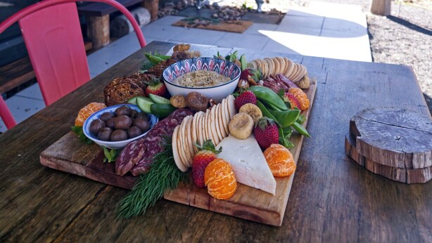 A wooden table with a charcuterie board, a bowl of dip, and a bathtub in the background. - Wake with the Kangaroos: Sunrise Cabin Escape in Mudgee (Frog Rock)