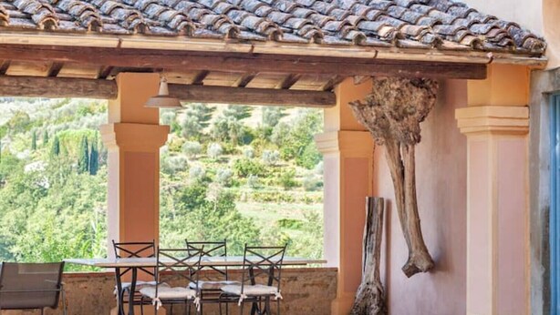 Un patio al aire libre con mesa y sillas, una pérgola y vistas a un paisaje verde.