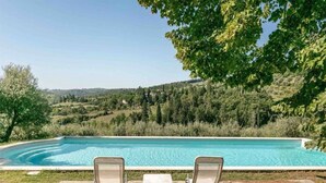 Piscina con dos sillas reclinables y una mesa, rodeada por un paisaje natural.