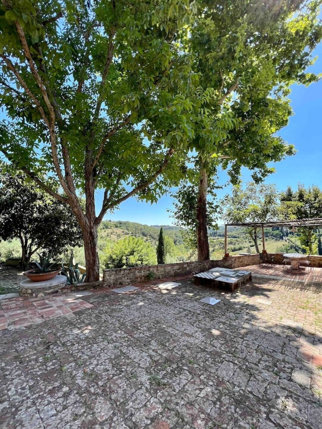 Un patio con suelo de piedra, una mesa y sillas bajo una pérgola.