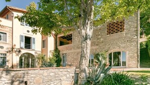 Un edificio tradicional con muros de piedra, ventanas arqueadas y un árbol en el patio.