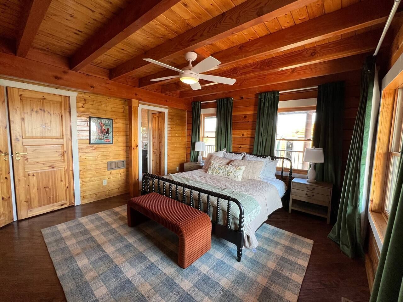 Un dormitorio de cabaña de madera con cama, banco, ventilador de techo y vistas al exterior.