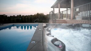 Una piscina con zona de hidromasaje, un espacio de estar cubierto y vistas a árboles al fondo.